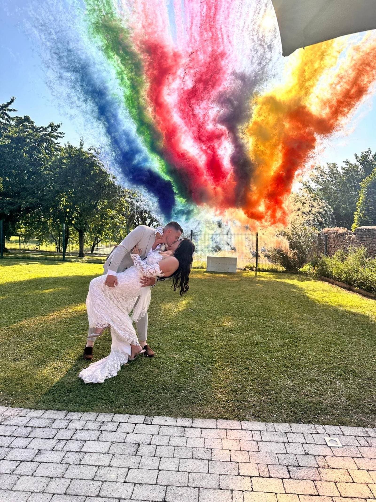 Couple de mariés s'embrassant devant des fumées colorées arc-en-ciel — feu d'artifice de jour